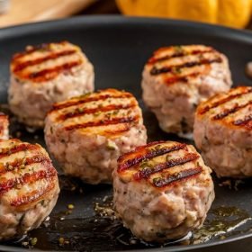 Close-up of turkey sausage patty ingredients: ground turkey, minced garlic, and seasonings like sage, thyme, and black pepper arranged on a table with a blurred chef in the background, creating a cooking atmosphere.