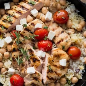 Greek chicken and lemon rice topped with lemon zest and sprigs of thyme.